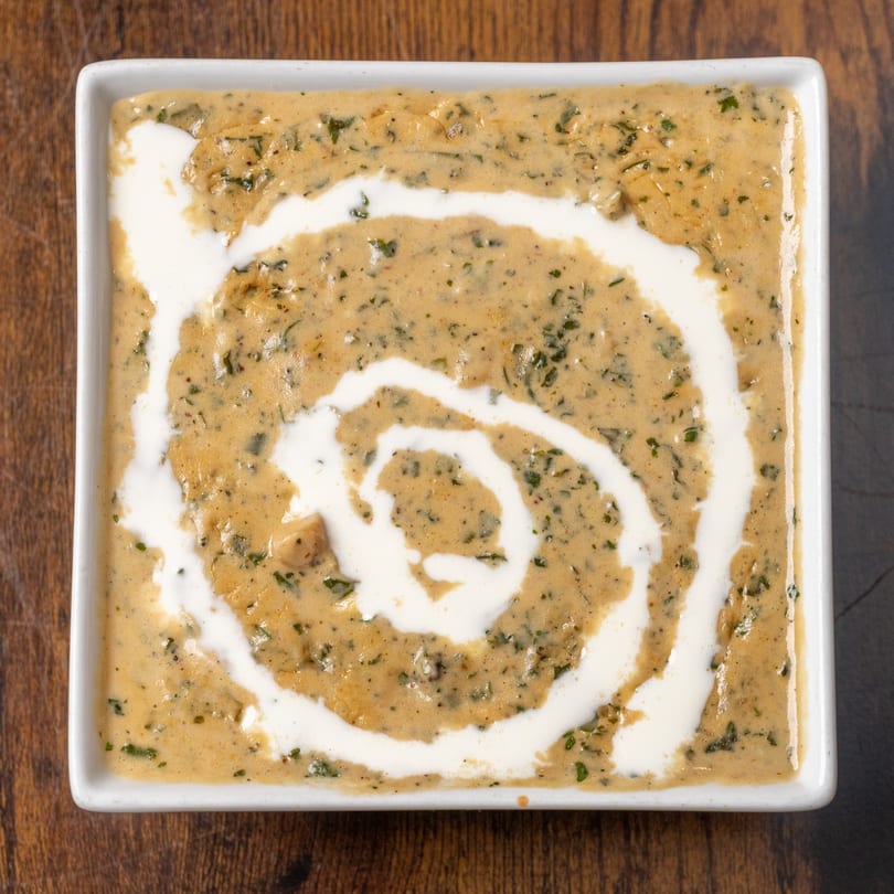 Creamy Indian curry with green herbs and a white cream swirl, served in a square white dish.