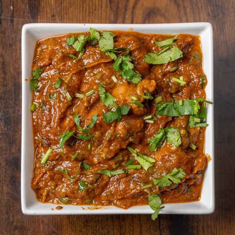 A close-up of Indian chicken curry in a white square bowl, garnished with fresh cilantro.