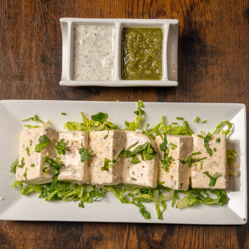 Indian Delight's paneer tikka, garnished with herbs and served with green chutney and raita.