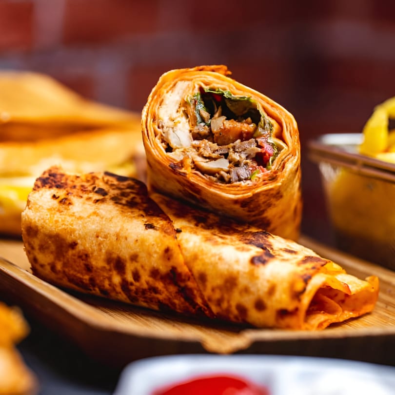 Two Indian Delight chicken shawarma wraps, one cut open to show the filling, on a wooden tray.