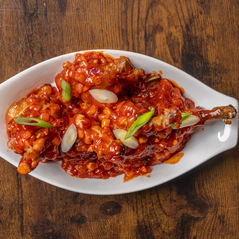 Indian Delight's chicken lollipops, coated in a vibrant red sauce and garnished with green onions.