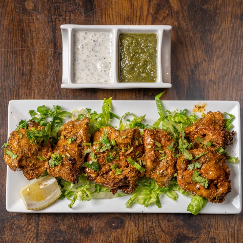 Indian Delight's chicken tikka, garnished with cilantro and lemon, served with two dipping sauces.