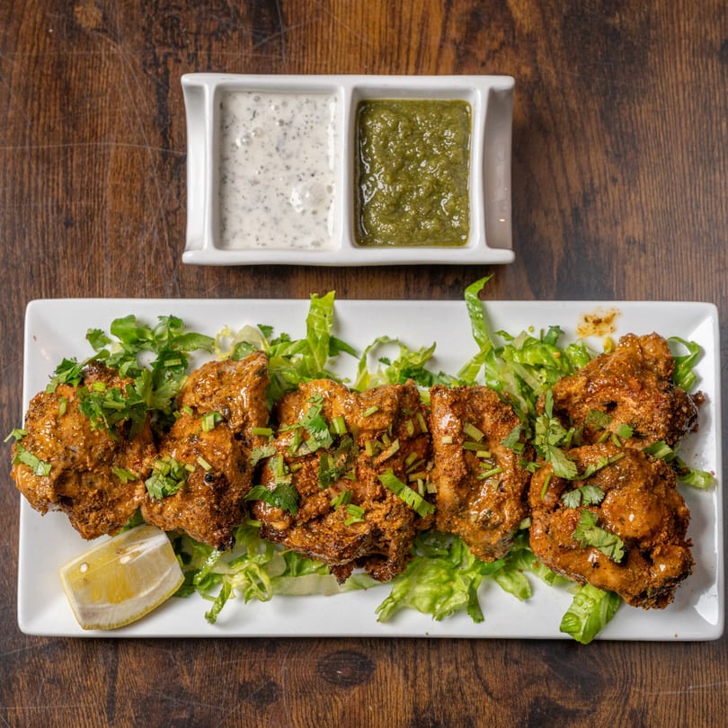 Indian Delight's chicken tikka, garnished with cilantro and lemon, served with two dipping sauces.