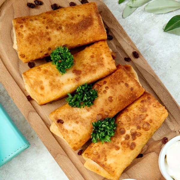 Four golden-brown Indian spring rolls, garnished with parsley, on a wooden board with raisins.
