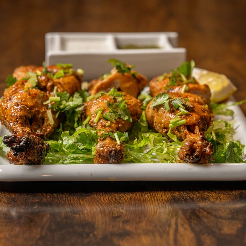 Indian Delight's chicken drumsticks, garnished with cilantro and served on a bed of lettuce with lemon.