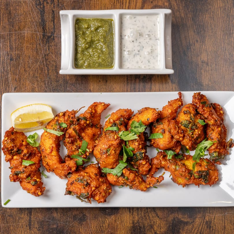Indian Delight's chicken pakora, garnished with cilantro and lemon, served with green and white dipping sauces.