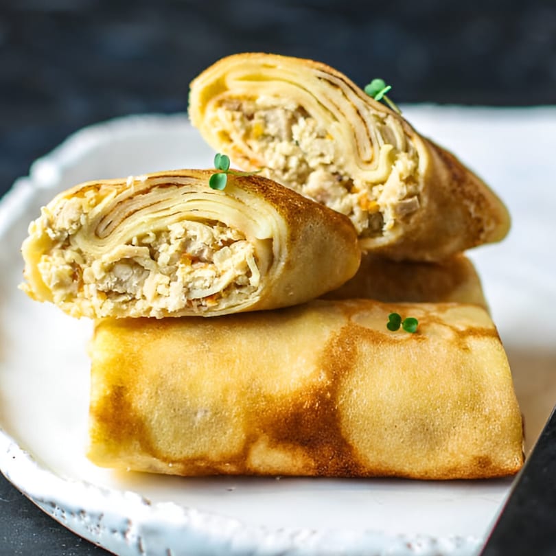 Three golden-brown Indian spring rolls, two cut open to reveal a savory filling, garnished with microgreens.